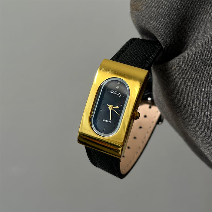 Gold wristwatch with black strap held by a gloved hand against a gray background