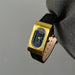 Gold wristwatch with black strap held by a gloved hand against a gray background