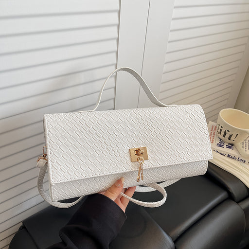 A white textured clutch handbag with a top handle and a gold clasp, held by a hand over a black leather sofa in front of white slatted doors.