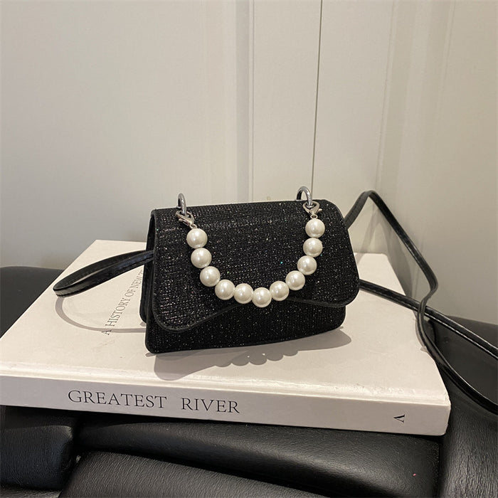 A small black glittery handbag with a pearl-bead strap, resting on a white book with the title 'GREATEST RIVER' on a dark leather surface.