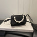 A small black glittery handbag with a pearl-bead strap, resting on a white book with the title 'GREATEST RIVER' on a dark leather surface.