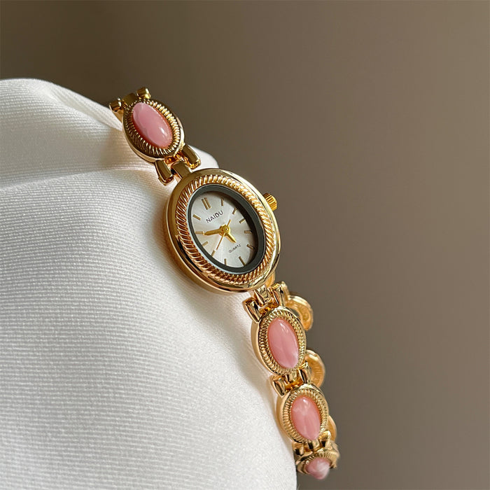 Gold watch with pink gemstones on a white cushion