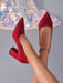 A pair of red suede pointed-toe pumps with block heels, shown on a model's feet against a gray background with a sequined chandelier decoration.