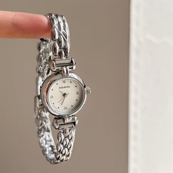 Silver watch with a textured band held by a finger against a neutral background