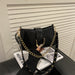 A black faux-leather shoulder bag with a gold-tone chain strap and gold studs, held by a hand over a magazine on a black leather surface.