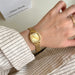 Gold watch on a wrist with a neutral background