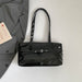 A glossy black patent leather shoulder bag with silver-tone hardware, laid flat on a light gray surface next to a gray blazer and a small card.