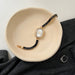 Gold watch with black beaded strap on a beige dish, gray fabric background