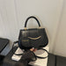 A black leather handbag with a top handle, gold-tone hardware, and a hanging circular charm that reads 'FASHION', shown resting on a white box with a hand holding the strap in a modern indoor setting.