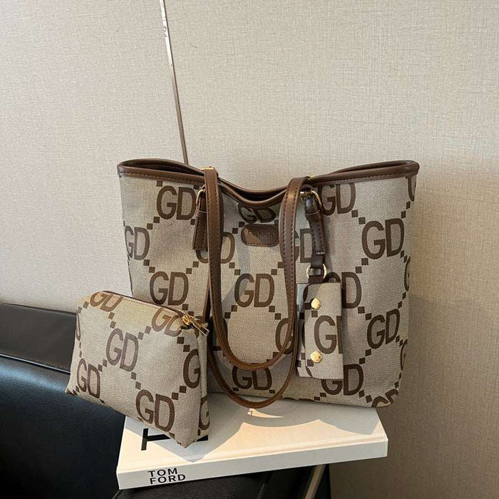 A beige tote bag with a brown monogram pattern and matching zip pouch, displayed on a white book on a black chair against a textured beige wall.