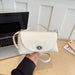 A hand holding a small off-white pebbled leather handbag with a top handle and silver hardware, set against a desk background with a laptop and books.