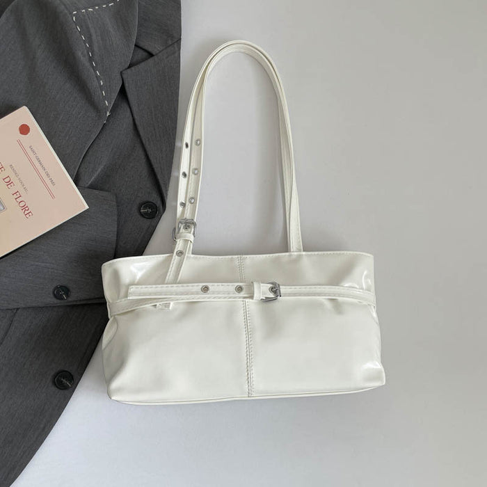 A glossy white faux-leather shoulder bag with silver-tone hardware, displayed on a light gray surface next to a dark gray blazer and a small pink card.