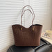 A brown leopard-print tote bag with two shoulder straps and small gold-tone hardware, placed on a black leather chair in front of white slatted doors. A magazine and a cup sit to the right.