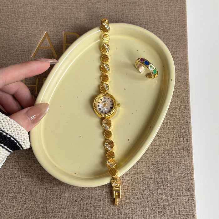 Gold bracelet and ring on a beige dish with a hand holding it, against a textured brown background.