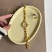 Gold bracelet and ring on a beige dish with a hand holding it, against a textured brown background.