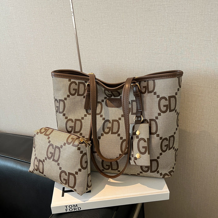 A beige tote bag with a brown monogram pattern and matching zip pouch, displayed on a white book on a black chair against a textured beige wall.