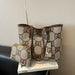 A beige tote bag with a brown monogram pattern and matching zip pouch, displayed on a white book on a black chair against a textured beige wall.