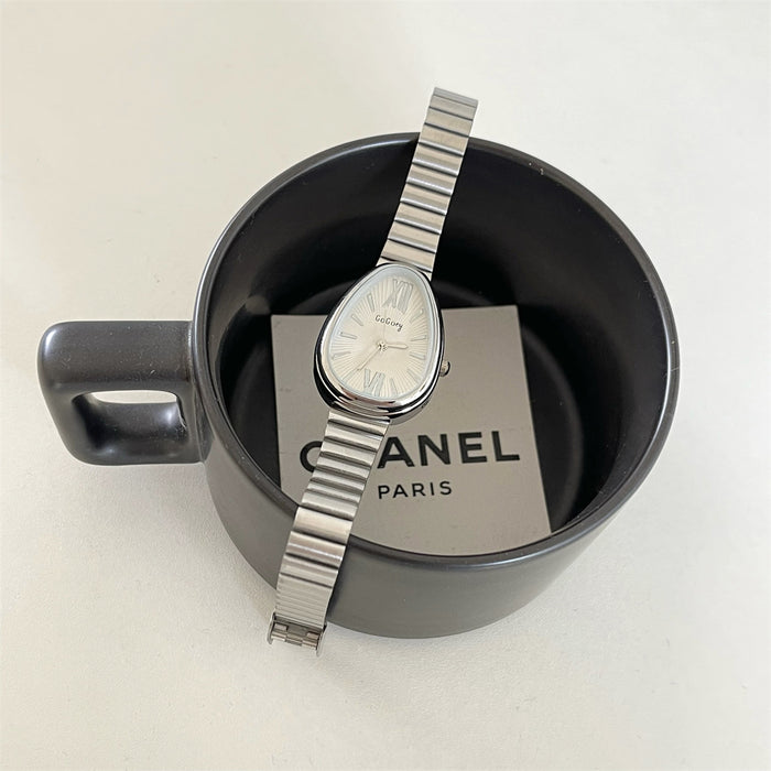 Silver watch with a Chanel Paris tag inside a black mug on a white background
