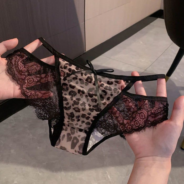 A pair of sheer leopard-print lace panties with black trim and floral lace side panels, held up by two hands against an indoor tiled floor background.