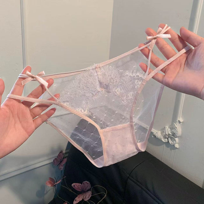 A pair of sheer mesh panties with a light pink lace pattern and matching pink ribbon bows at the side straps, held up by two hands against an indoor background.