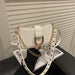 A white faux leather shoulder bag with a gold-tone metal D-ring clasp and a gold chain strap, styled on a black leather surface with a magazine in the background.
