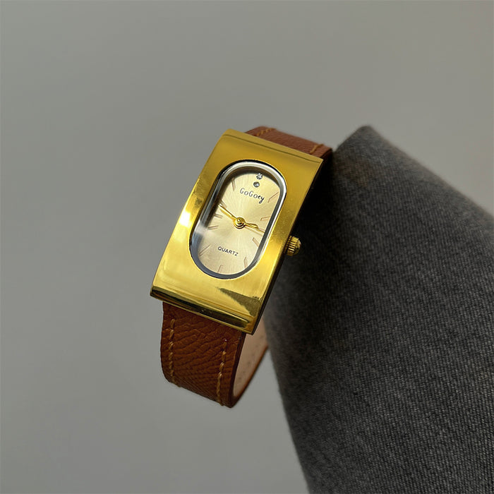 A vintage-style wristwatch with a polished gold-tone rectangular case, oval dial, and brown leather strap, displayed on a gray fabric surface against a neutral gray background.
