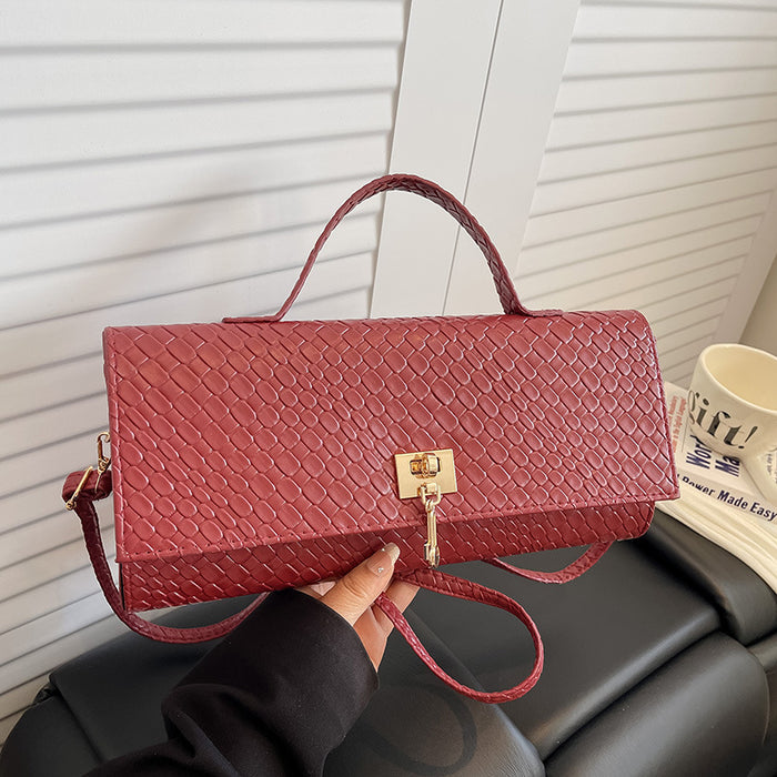 A textured red handbag with a top handle and a gold clasp, held by a hand in front of a white slatted door and a black leather chair.