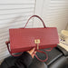 A textured red handbag with a top handle and a gold clasp, held by a hand in front of a white slatted door and a black leather chair.
