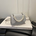 A small light gray woven handbag with a pearl bead strap, resting on a white book with the title 'GREATEST RIVER' on a black leather chair.