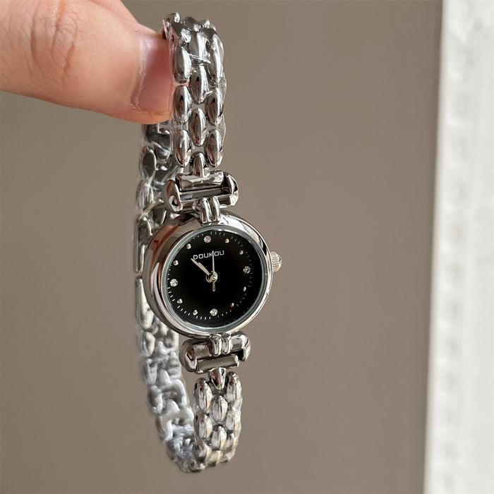 Silver chain watch with black dial held by a hand against a neutral background