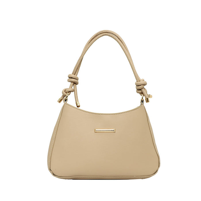 A light beige shoulder bag with a curved top handle, knotted details at the base of the handle, and a small horizontal gold-tone metal accent on the front, shown against a plain white background.