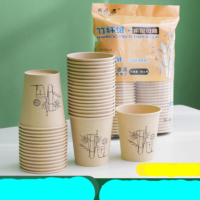 Bamboo fiber paper cup set with a large printed packaging bag and multiple stacks of disposable cups on a white surface against a green wall. Chinese text appears on the bag and as an overlay banner.