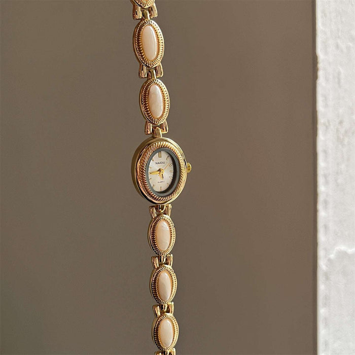 Gold watch with decorative links on a neutral background