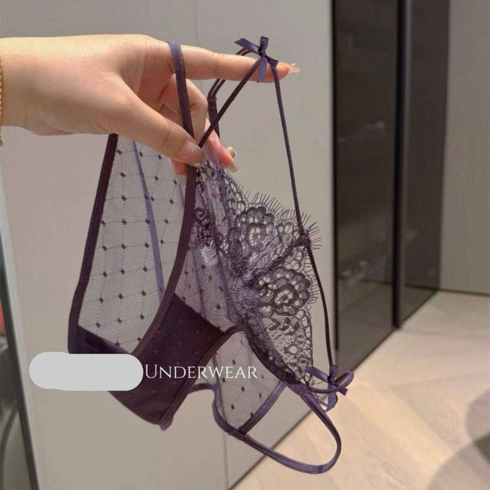 A hand holds up a dark purple lace and mesh panties set with adjustable straps and bow details, set against an indoor background with a visible SANZHIMAO UNDERWEAR watermark.