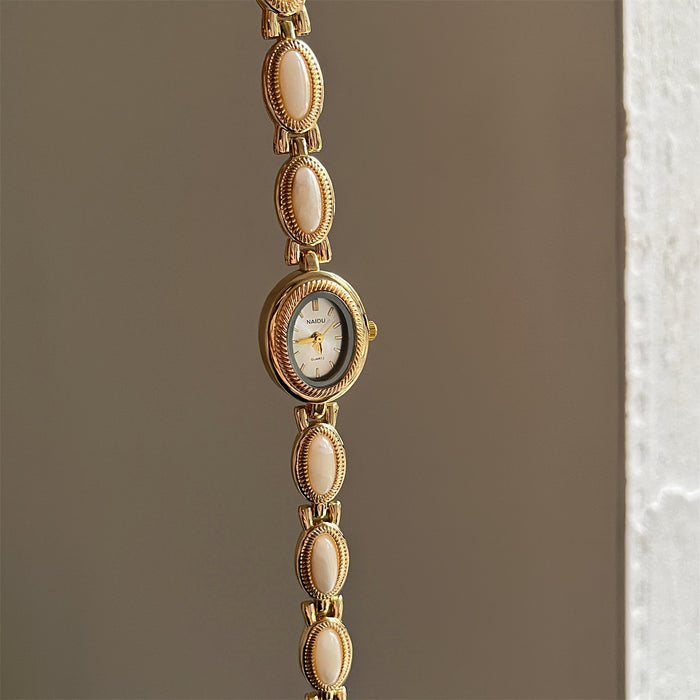 Gold watch with decorative links on a neutral background