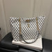 A white tote bag with a black repeating monogram pattern and gold-tone chain handles, displayed on a white book resting on a black leather chair.