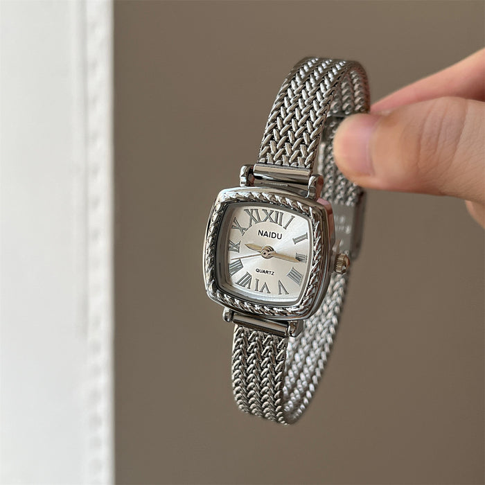 Silver watch with mesh band held by a hand against a neutral background