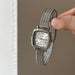 Silver watch with mesh band held by a hand against a neutral background