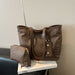 A brown monogram tote bag with matching zip pouch, displayed on a white book against a neutral textured wall.