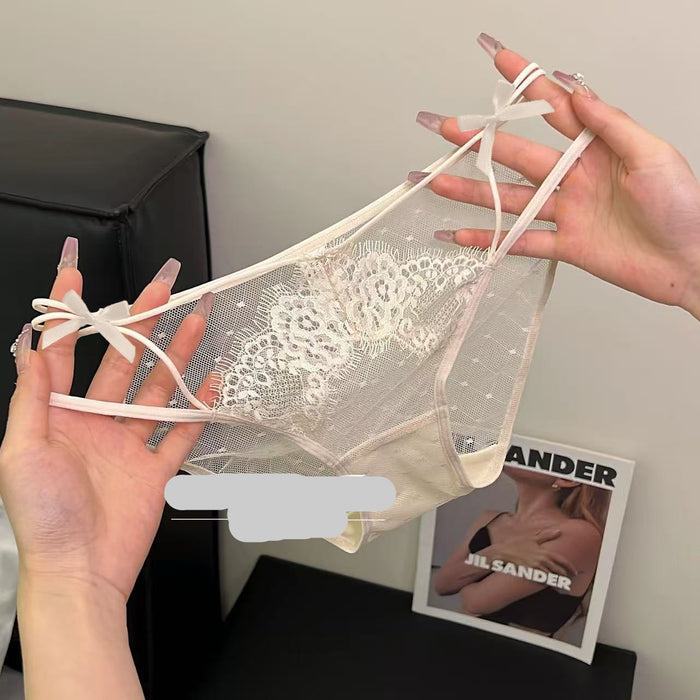 A pair of sheer white lace panties with white elastic straps and bow details, held up by two hands against a neutral indoor background.
