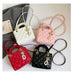 Four quilted mini handbags in white, pink, red, and black, arranged on a light beige surface with a gray jacket and a small book in the background. Each bag has a top handle, a long shoulder strap, a diamond-quilted pattern, gold-tone hardware, and a pearl tassel charm.