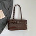 A glossy dark brown leather shoulder bag with silver-tone hardware, displayed on a light gray surface next to a gray blazer and a small card.