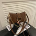 A brown faux-leather shoulder bag with a gold-tone chain strap and gold studs, held by a hand over a magazine on a black table.