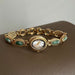 Gold bracelet watch with green gemstones on a brown surface