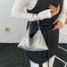 A person wearing a white long-sleeve top and a black apron-style garment holds a silver sequined slouchy shoulder bag with thin metallic handles.