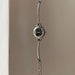 A silver-tone metal link watch with a round black dial and small crystal hour markers, hanging against a plain beige wall.