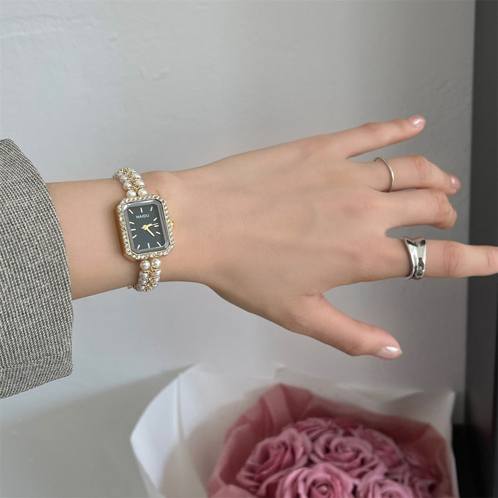 Hand wearing a decorative watch with a ring, against a neutral background.