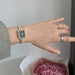 Hand wearing a decorative watch with a ring, against a neutral background.