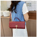 A woman wearing a blue knit vest over a white t-shirt and white skirt carries a red textured crocodile-embossed handbag with a gold clasp in a kitchen setting.