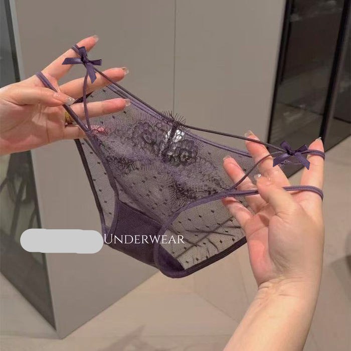 A pair of sheer purple lace thong underwear with small bow details on the side straps, held up by two hands against an indoor background. 